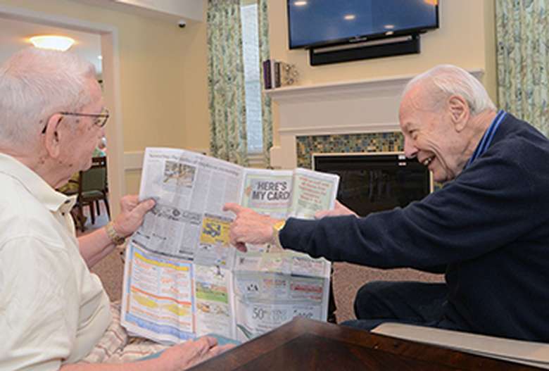 two elderly men, and one is pointing at a newspaper