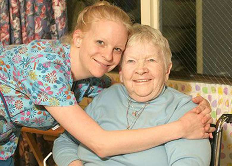 a woman in a colorful shirt hugging an elderly woman who is sitting down