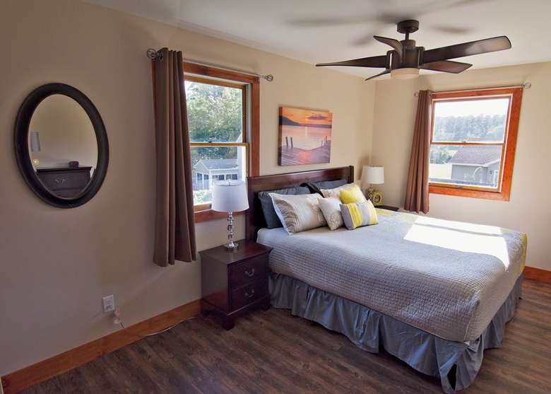 a bedroom with two windows, a round mirror on the wall, and one bed