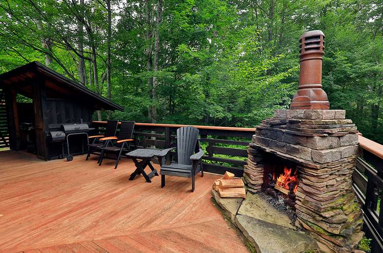 fireplace on a wooden patio deck near chairs and a grill
