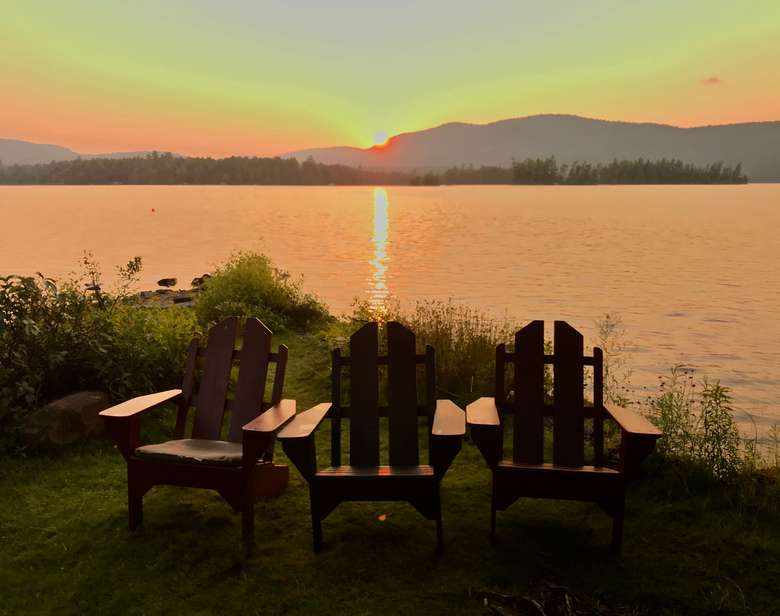 three Adirondack chairs with a sunset in the background