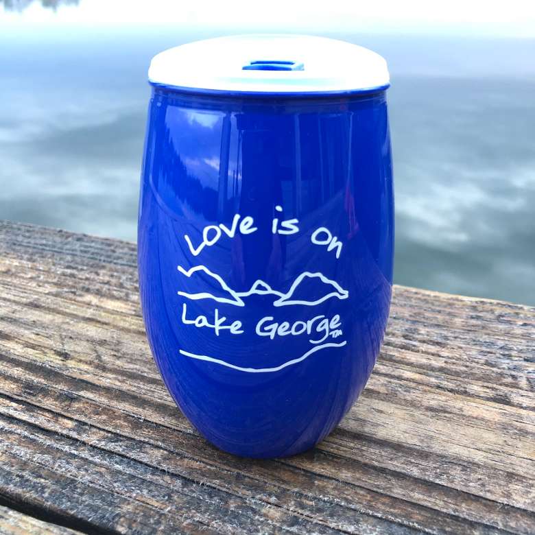 Love is on Lake George text over/under our Lake and mountain scene. Blue cup with whiter lettering and lid.