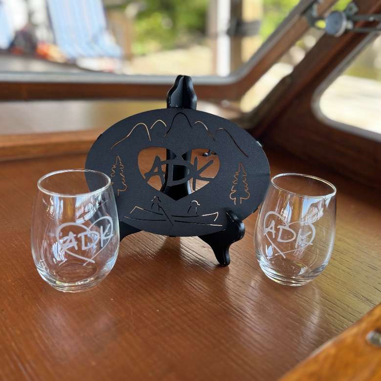 ADK Gift Set that includes two Clear Glass stemless wine glasses with our ADK in a heart logo hand sand blasted on them and  paired with a black metal ADK Trivet.