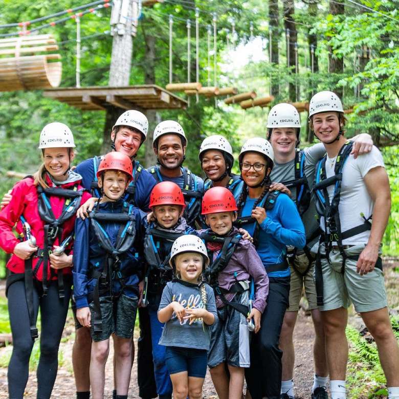 11 adults and kids wearing gear for an aerial adventure course