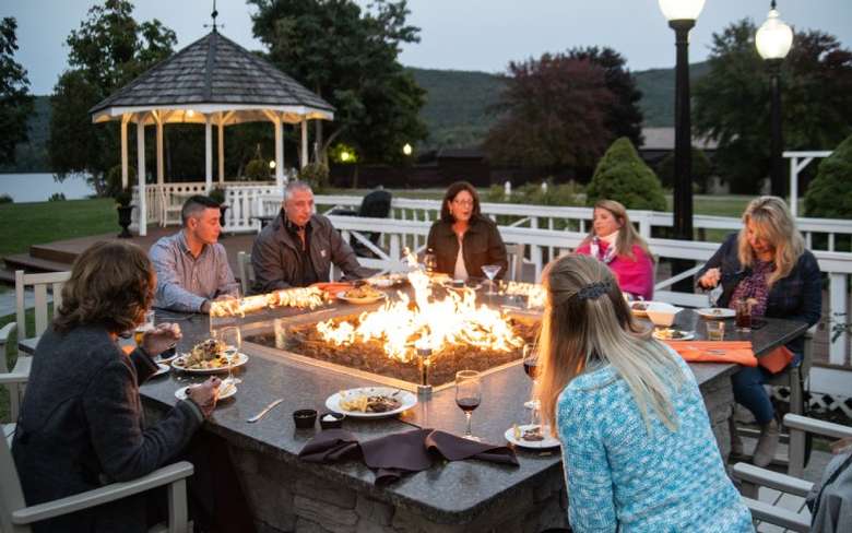 people seated around a fire pit with plates of food in front of them
