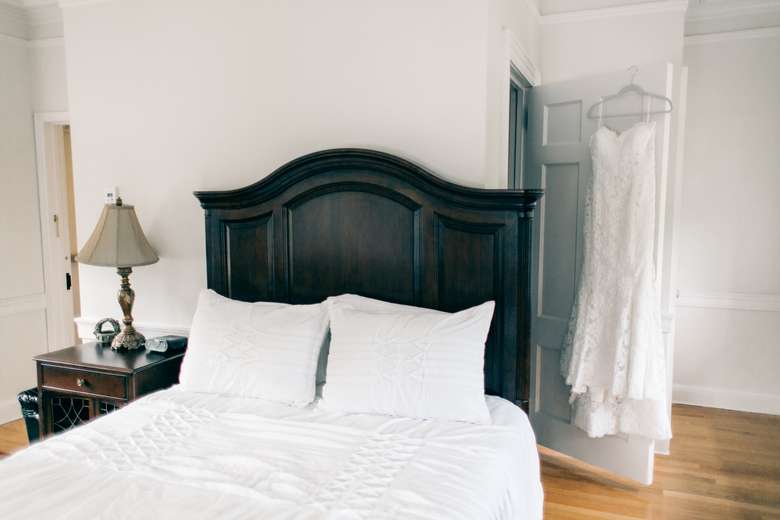 bed with wedding dress hung up on the closet door