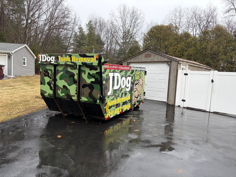 JDog Junk Removal dumpster outside a garage shed