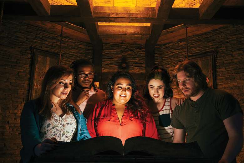 five people standing around a book in a fake tomb room