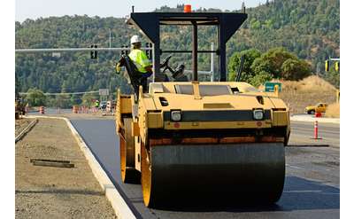 a paving construction vehicle and worker at the wheel