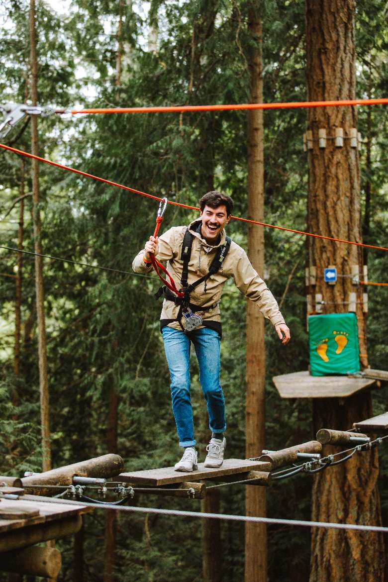 man walking across wooden platforms in a treetop course