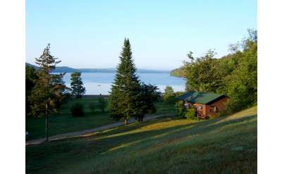 view of grassy lawn, a cabin, and a lake in the distance