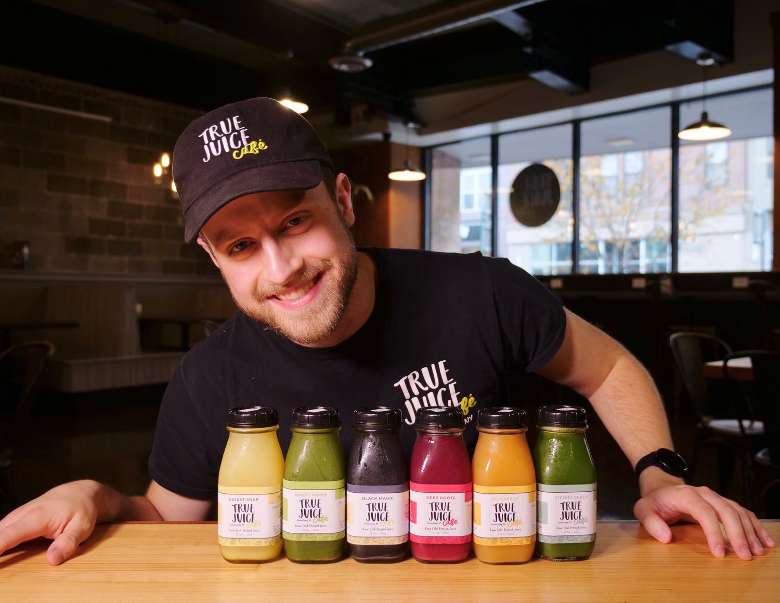 man smiling near row of juice bottles