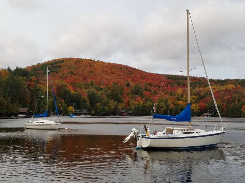 sailboats on calm water with fall colors on trees in the background