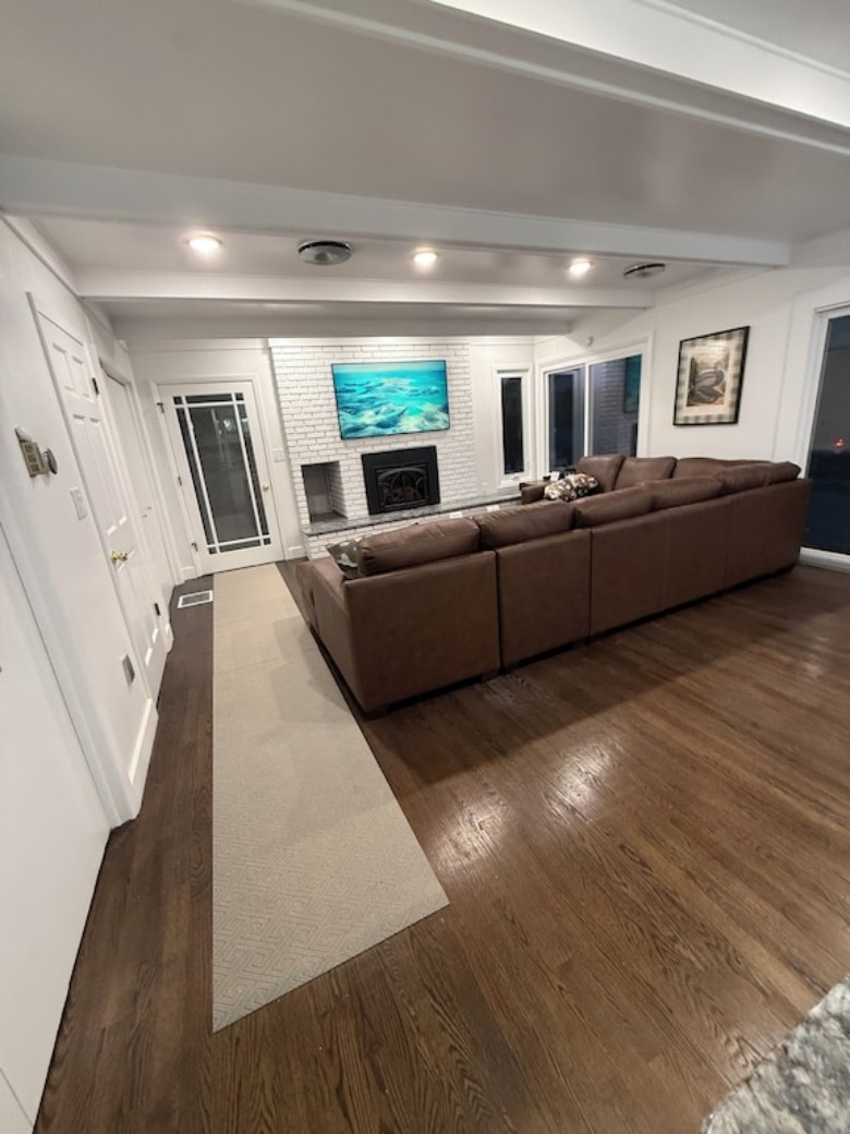 Formal living room with new sectional furniture, 65 inch Smart Apple TV, Juke Audio system, and decor. Windows on right side and sliding screen door to outdoor patio. Room is next to entrance from side door by garage and driveway