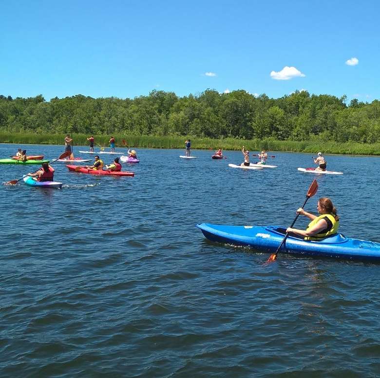 large group of kayakers and stand up paddleboarders on a waterway during a sunny day with blue sky