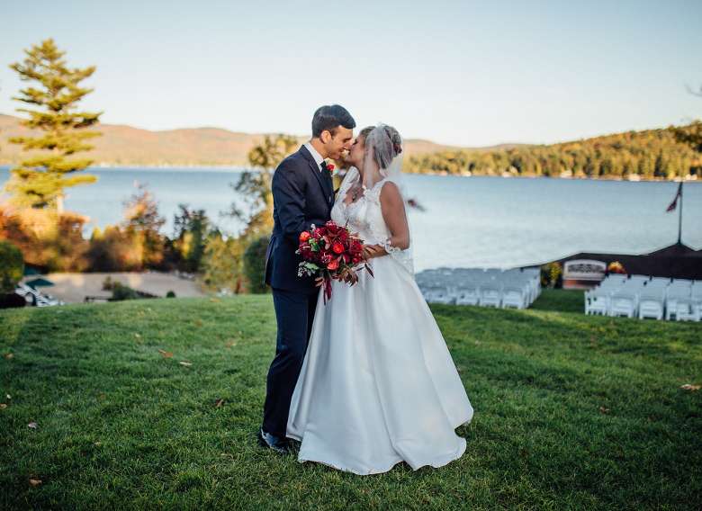 bride and groom embracing on a grassy lawn with a lake backdrop