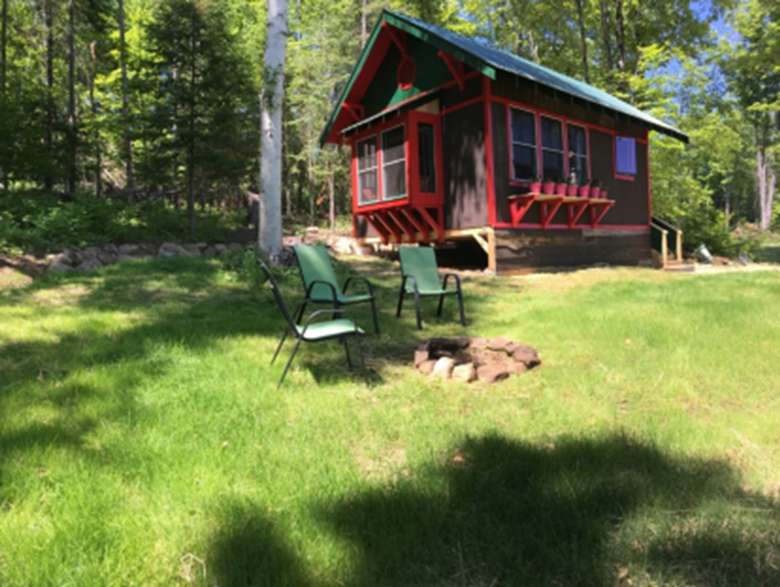 exterior of a dark brown cabin with chairs near a fire pit