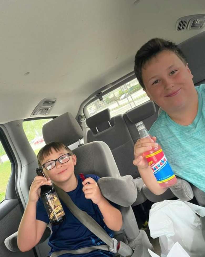 two kids holding up bottles of soda pop in a car