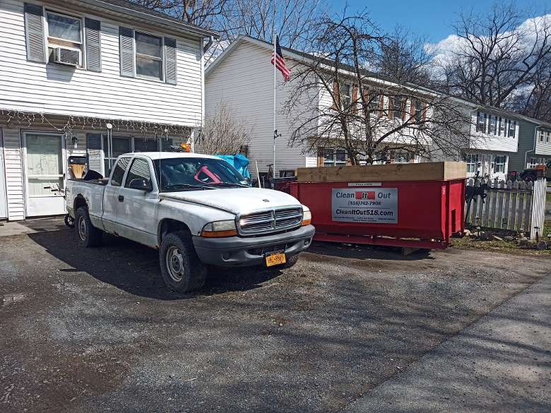 red dumpster by a white truck outside of a house