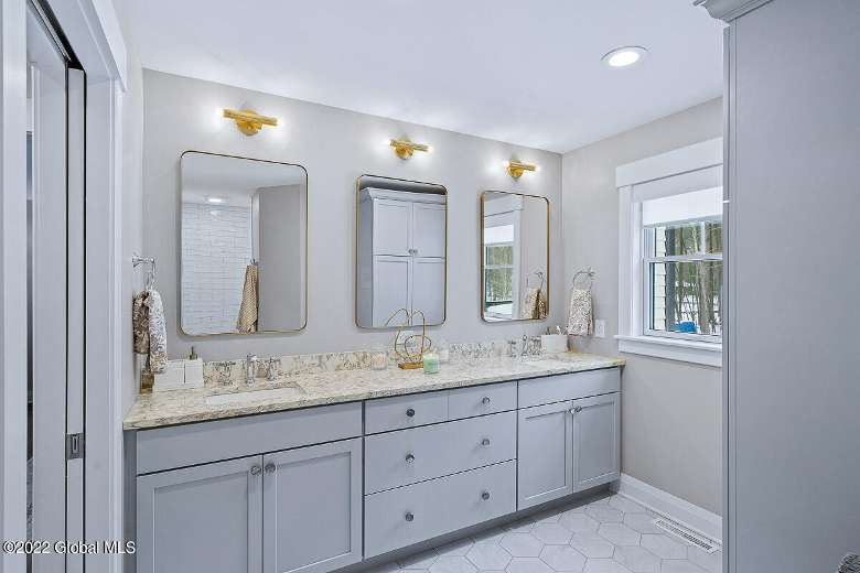 brightly lit bathroom with a large cabinet with a sink and three mirrors above it