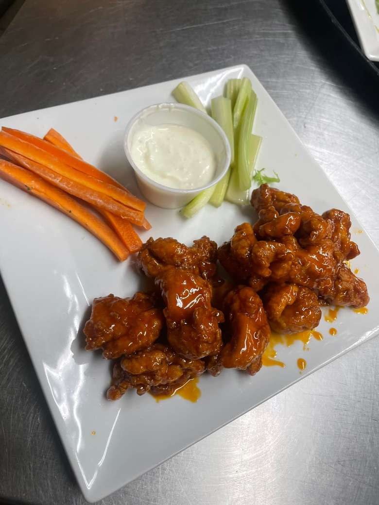 a plate with boneless wings, carrots, celery, and dip