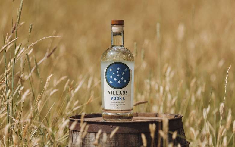 a bottle of Village Vodka on a barrel in a field