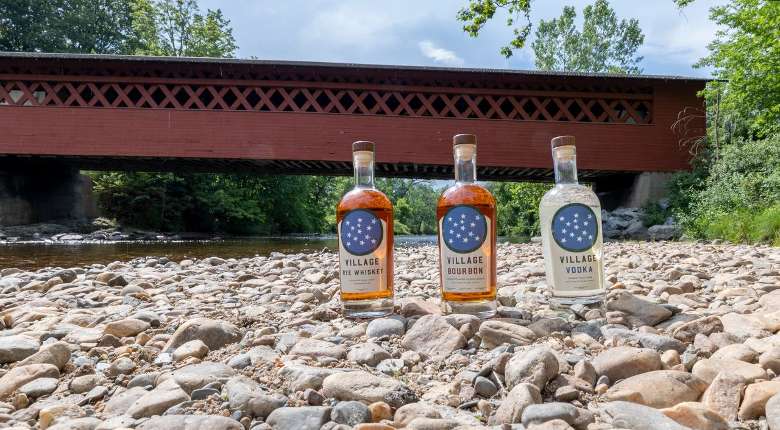three bottles of craft spirits on rocks near a red covered bridge