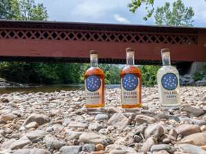 three bottles of craft spirits on rocks near a red covered bridge