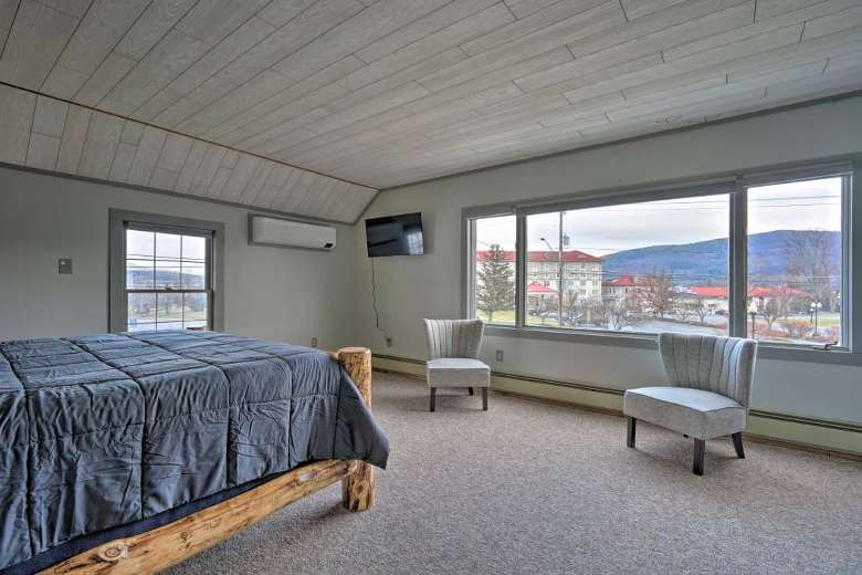 a large bedroom with a bed, two chairs, and big windows with a view of a hotel and mountains