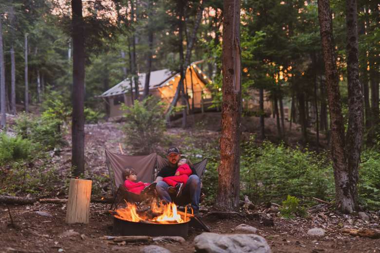 father sitting with kids around a campfire with glamping tent in the background