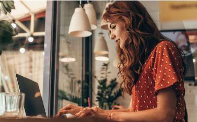 woman in orange shirt typing at a laptop