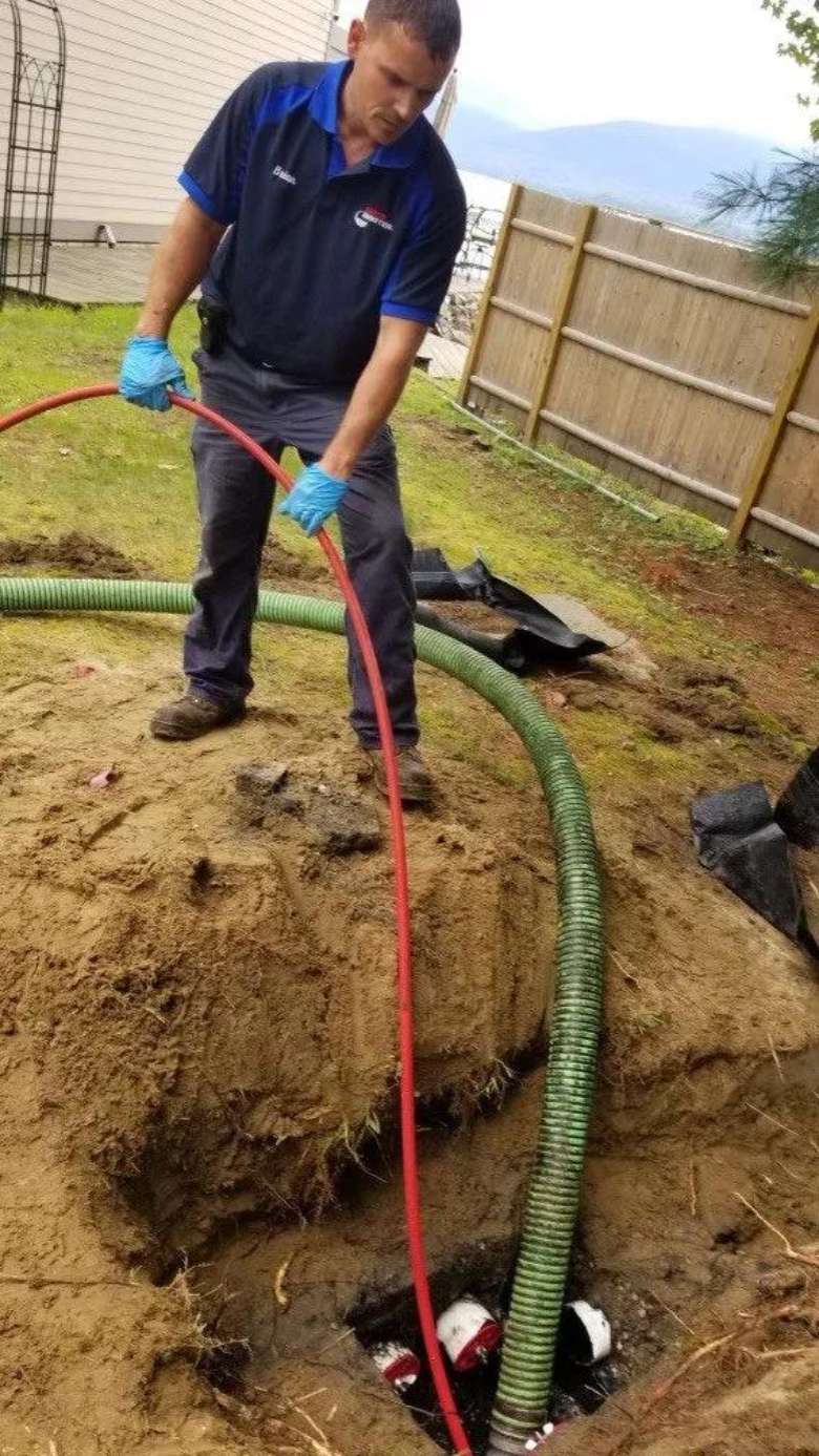 man holding red pipe into a septic tank