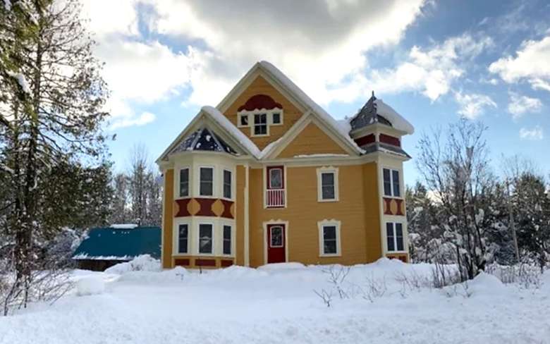 a large yellow colored Victorian home surrounded by snow
