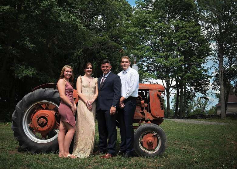 bride, groom, best man, and best woman standing by a red tractor
