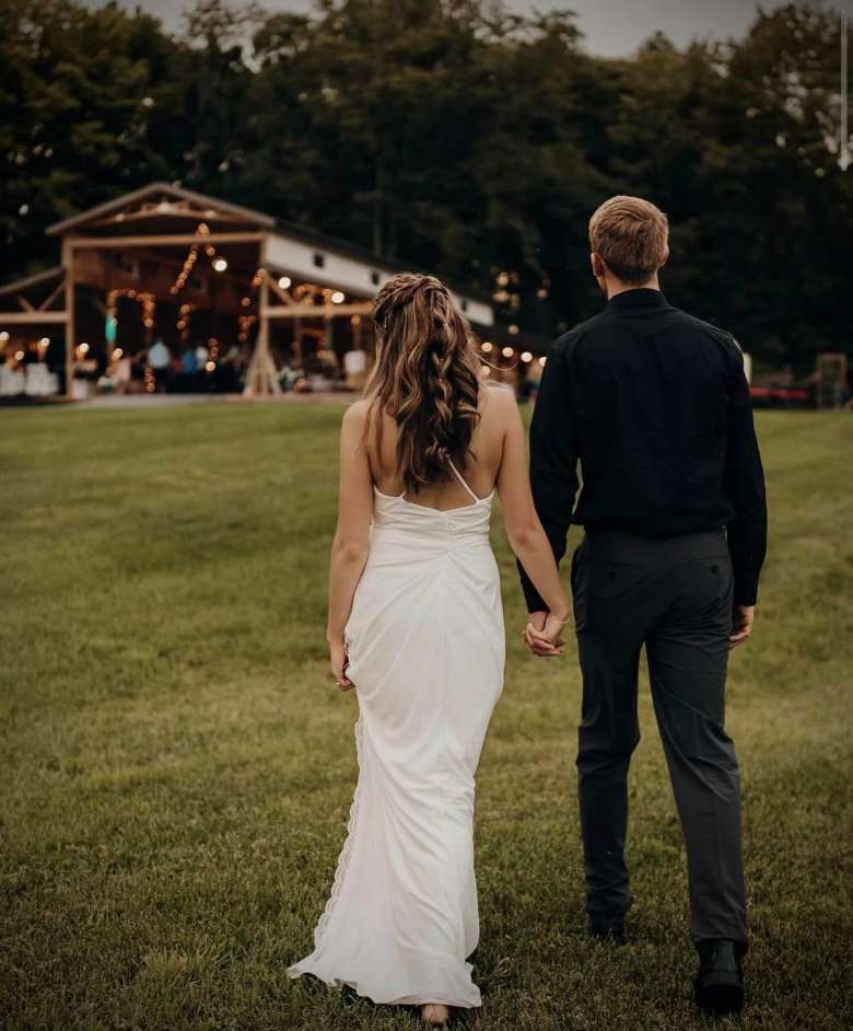 bride and groom walking hand in hand toward a barn venue