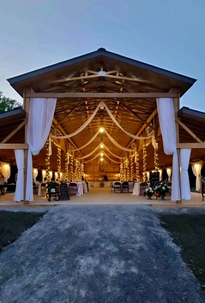 view of rustic wedding barn with lights and tables in the evening