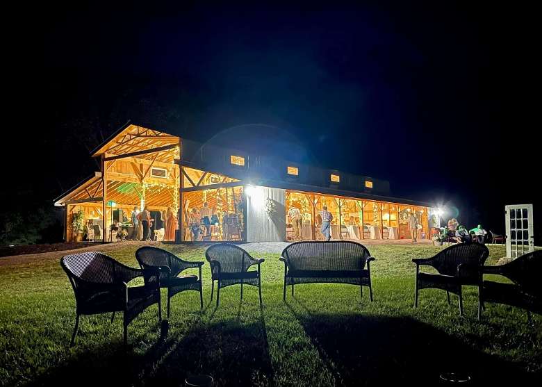 side view of large rustic wedding barn with lights on at night