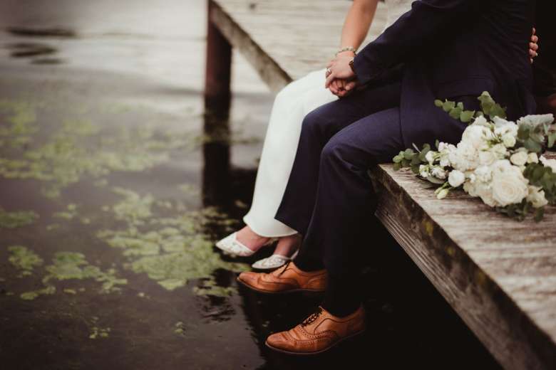 a bride and groom sitting on a wooden dock