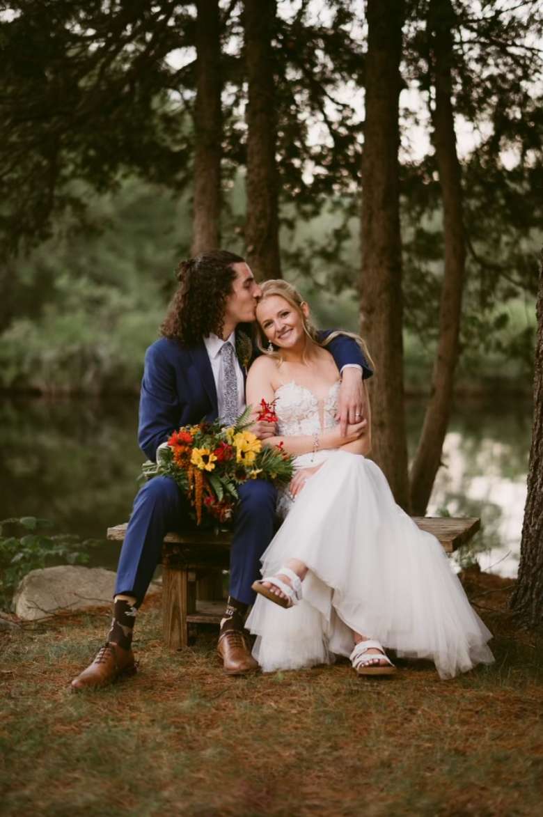 bride and groom posing for photo by a wooded shoreline