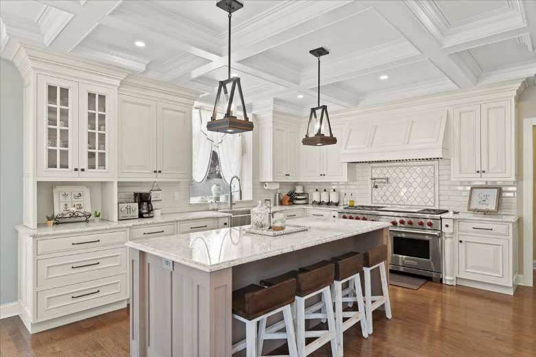 a large kitchen with an island and stools, white cabinets, hanging lights, and ovens