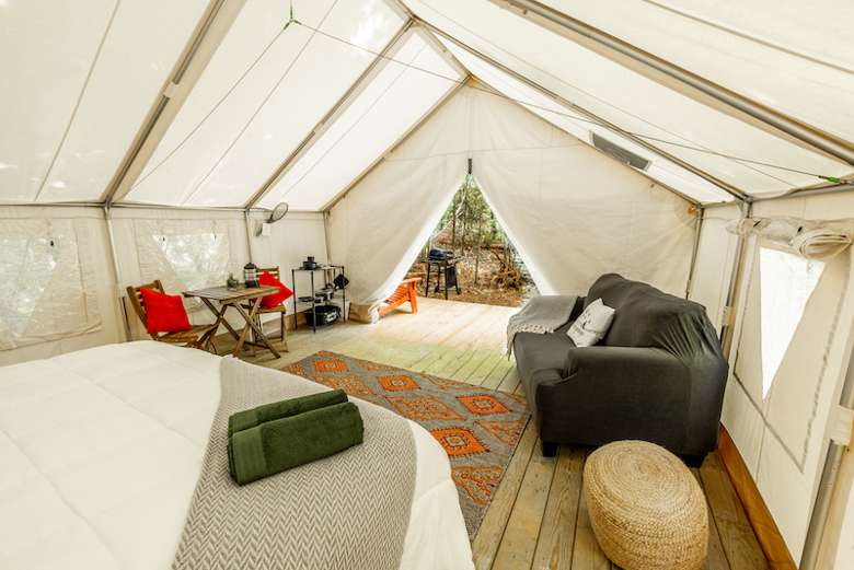 inside of a large glamping tent with a bed, couch, and table and chairs