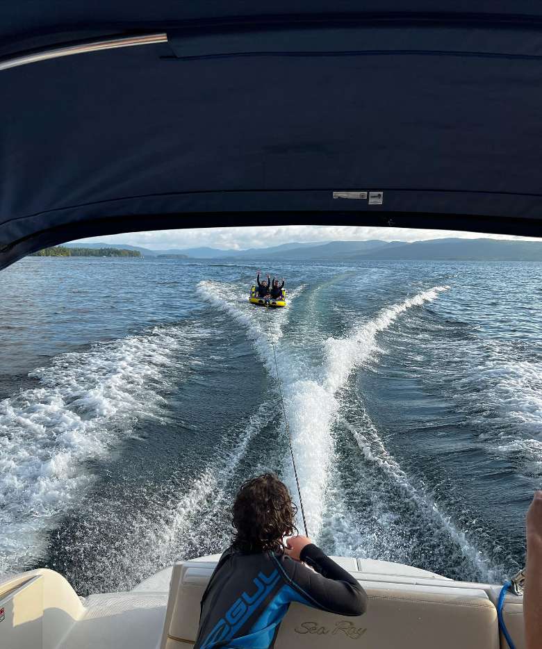 two people tubing while connected to a motorboat as someone watches