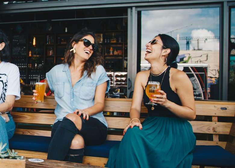 two women holding beers sitting outside laughing