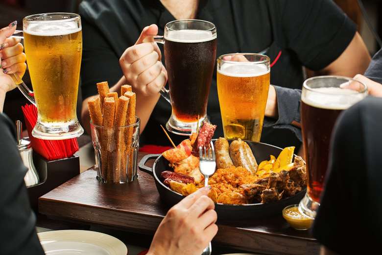 people holding beers and eating food at a table