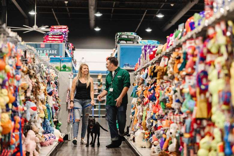 pet store employee, woman, and dog walking down an aisle