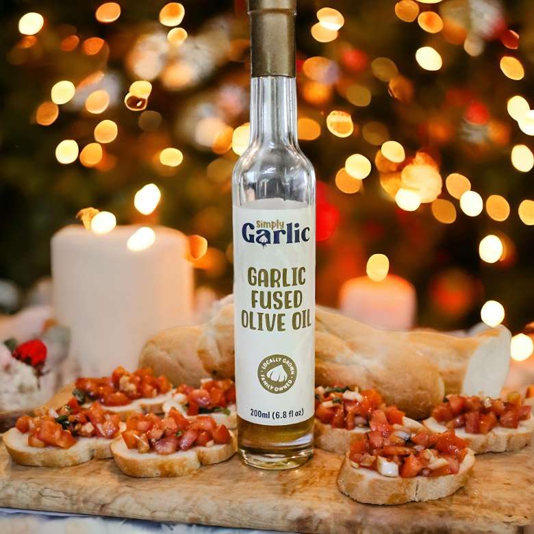 garlic infused olive oil bottle next to bruschetta with christmas candles and tree in background