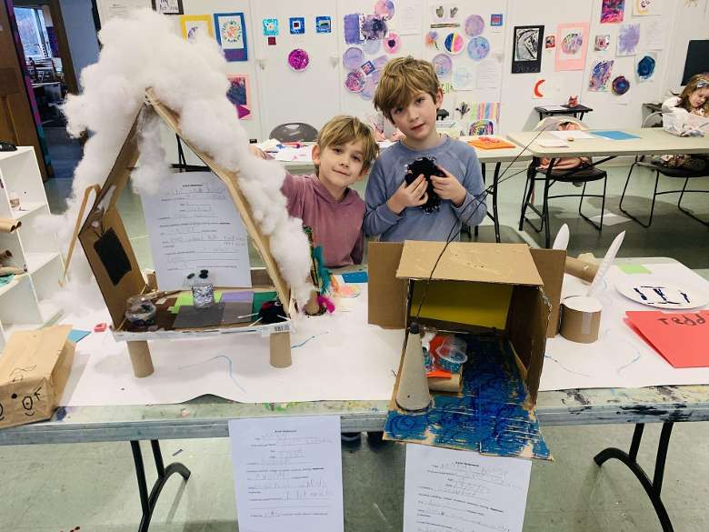 two children standing behind their art creations