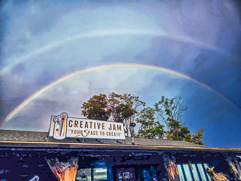 Double rainbow in a blue sky over the Creative Jam sign