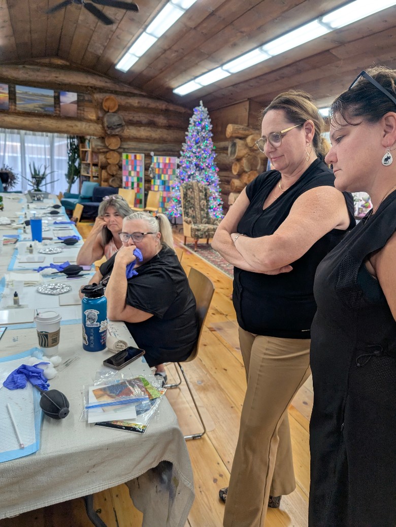 women watching a craft demonstration in a log cabin