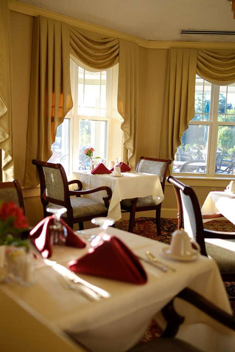 upscale dining room with white tablecloths, red napkins, long curtains, and padded chairs with arm rests